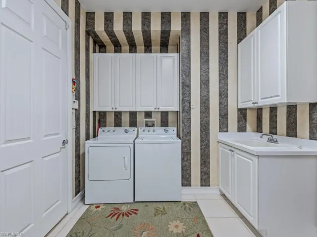 Laundry area with washing machine and clothes dryer, sink, light tile patterned floors, and cabinets