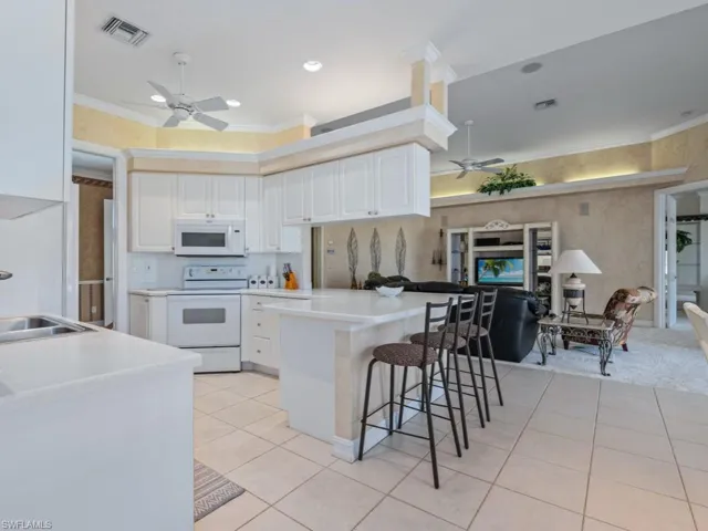 Kitchen featuring white cabinets, light tile patterned floors, white appliances, and crown molding