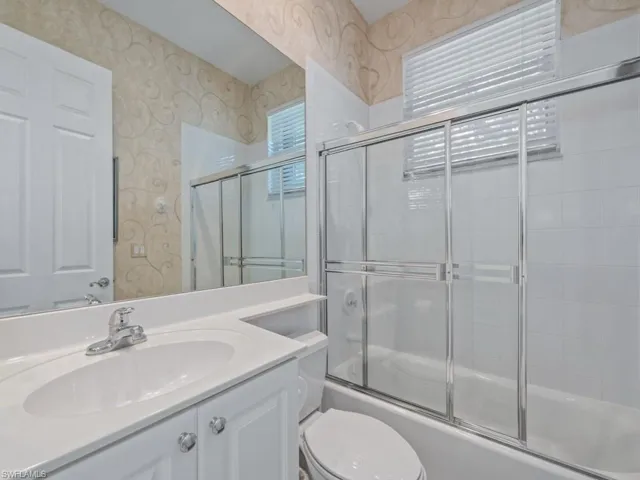 Full bathroom featuring vanity, toilet, and bath / shower combo with glass door