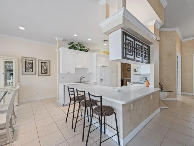 Kitchen featuring a breakfast bar, white appliances, white cabinets, sink, and ornamental molding