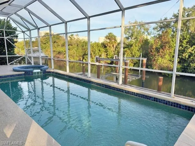 View of swimming pool featuring glass enclosure and an in ground hot tub