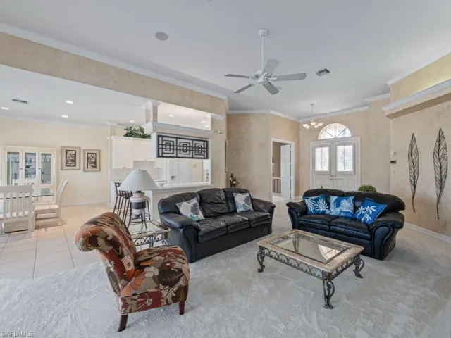 Tiled living room with ceiling fan with notable chandelier, ornamental molding, and french doors