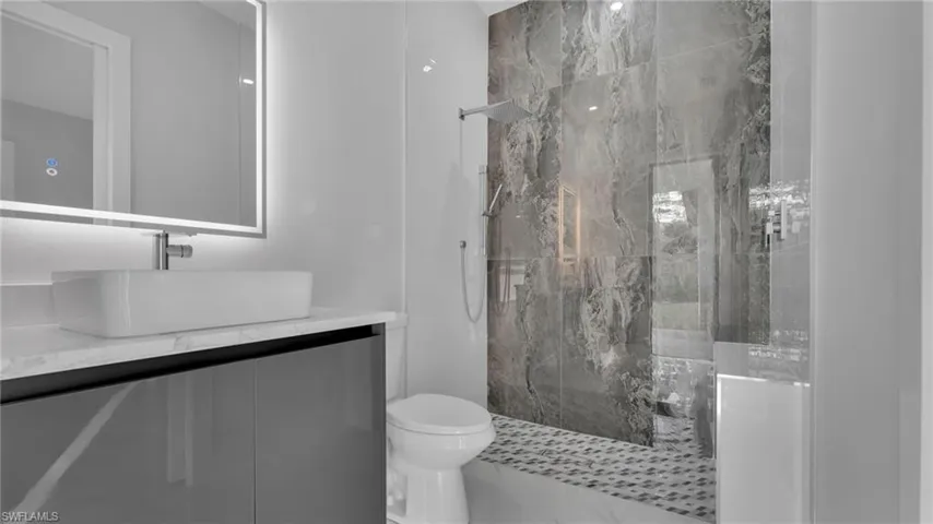Bathroom featuring toilet, vanity, and a tile shower