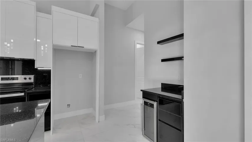 Kitchen with stainless steel electric range, dark stone counters, white cabinets, beverage cooler, and decorative backsplash