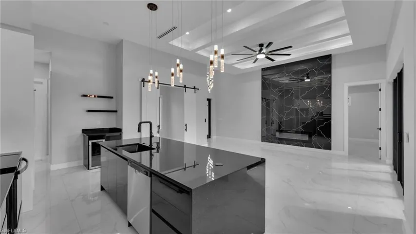 Kitchen featuring a large island with sink, decorative light fixtures, a tray ceiling, and sink