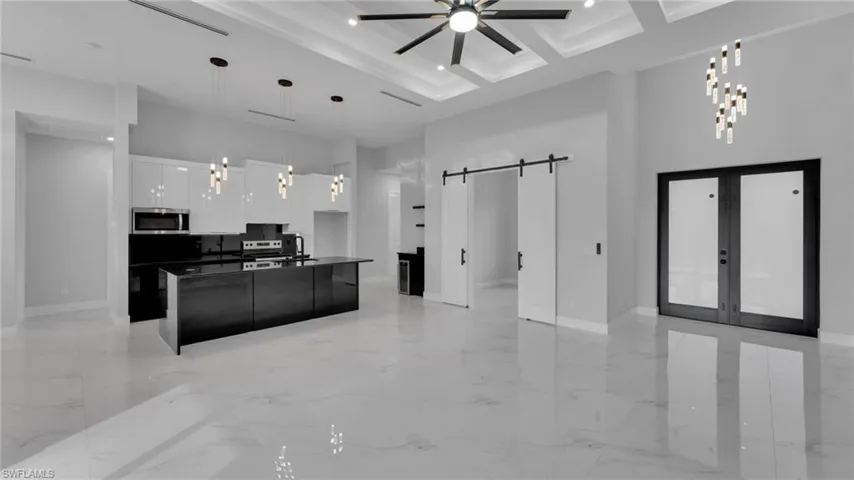 Kitchen with hanging light fixtures, a barn door, white cabinets, an island with sink, and french doors