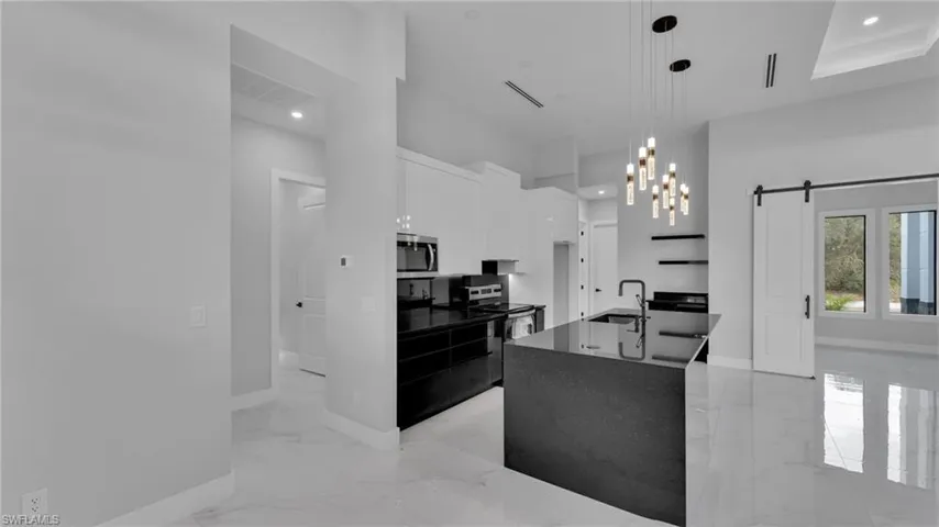 Kitchen featuring a center island with sink, appliances with stainless steel finishes, pendant lighting, white cabinetry, and a barn door