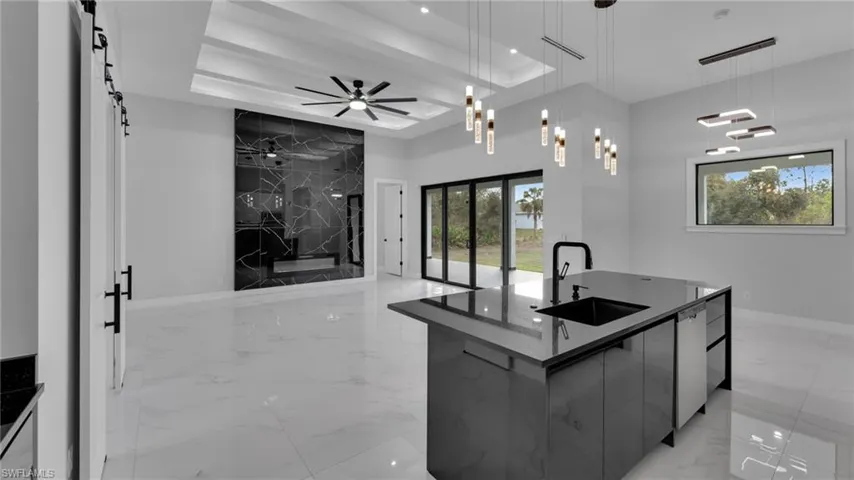 Kitchen featuring hanging light fixtures, a large island with sink, sink, a tray ceiling, and stainless steel dishwasher