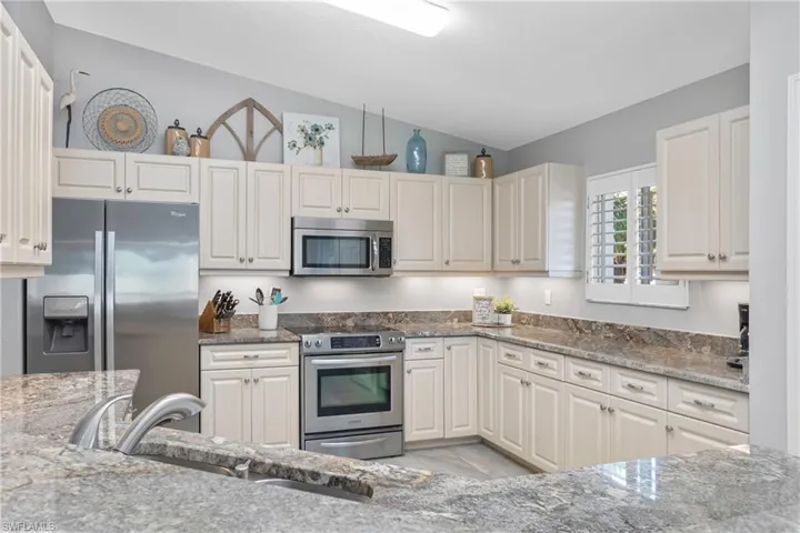 Kitchen with a sink, stone counters, appliances with stainless steel finishes, and vaulted ceiling