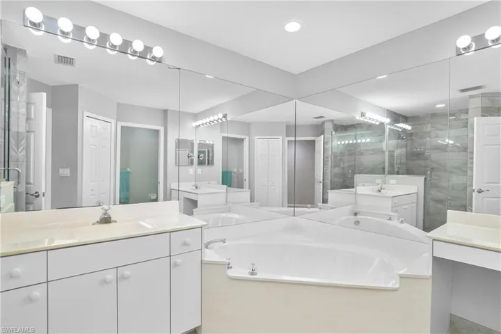 Bathroom featuring visible vents, two vanities, a sink, a shower stall, and a bath