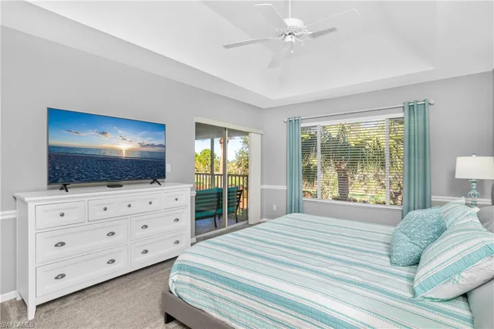 Bedroom with access to exterior, light colored carpet, a tray ceiling, and ceiling fan