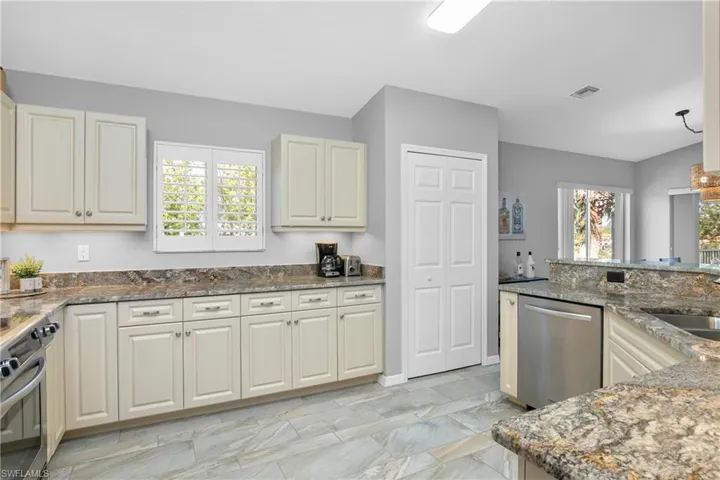 Kitchen featuring stainless steel dishwasher, stove, dark stone countertops, and visible vents