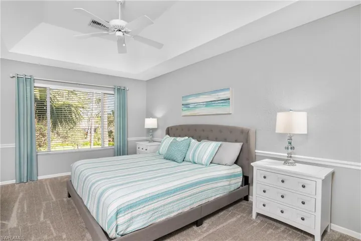 Bedroom with baseboards, a raised ceiling, light colored carpet, and ceiling fan