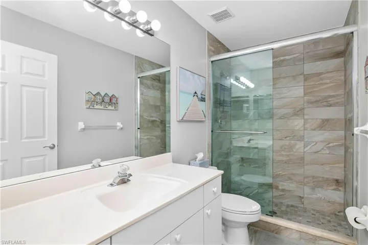 Bathroom featuring visible vents, toilet, a stall shower, and vanity