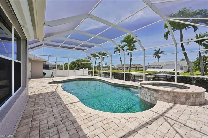 View of pool with a water view, glass enclosure, a patio, and a pool with connected hot tub