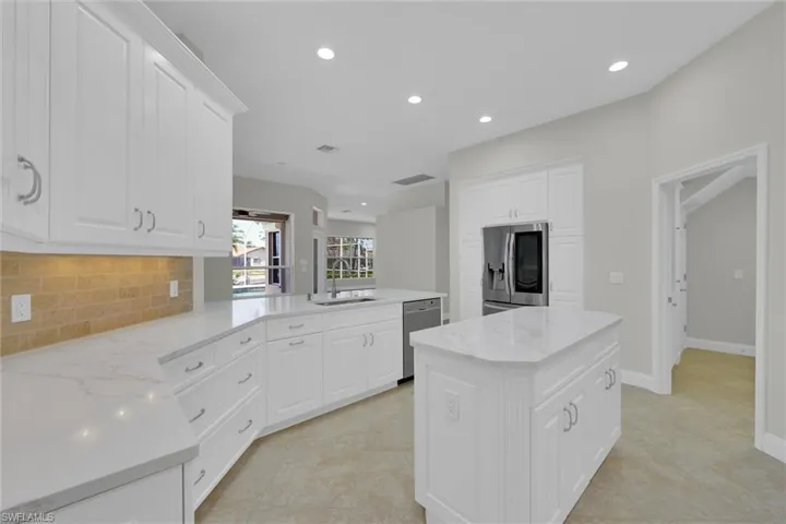 Kitchen with a sink, a peninsula, backsplash, white cabinets, and appliances with stainless steel finishes