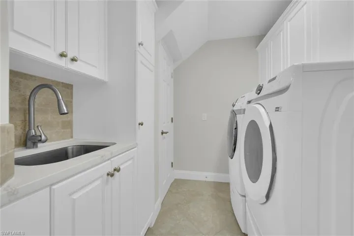 Laundry room with cabinet space, washing machine and dryer, baseboards, and a sink