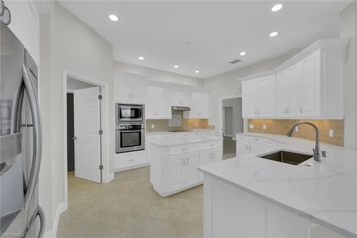 Kitchen featuring a sink, stainless steel appliances, under cabinet range hood, backsplash, and white cabinets