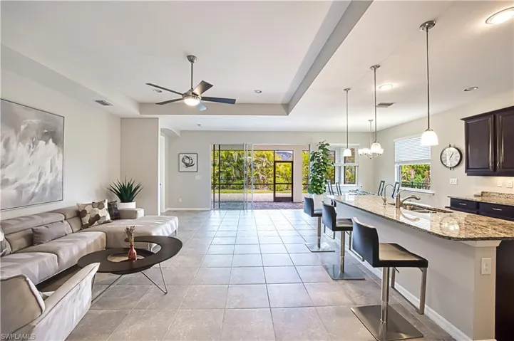 Tiled living room with sink, a tray ceiling, and ceiling fan with notable chandelier