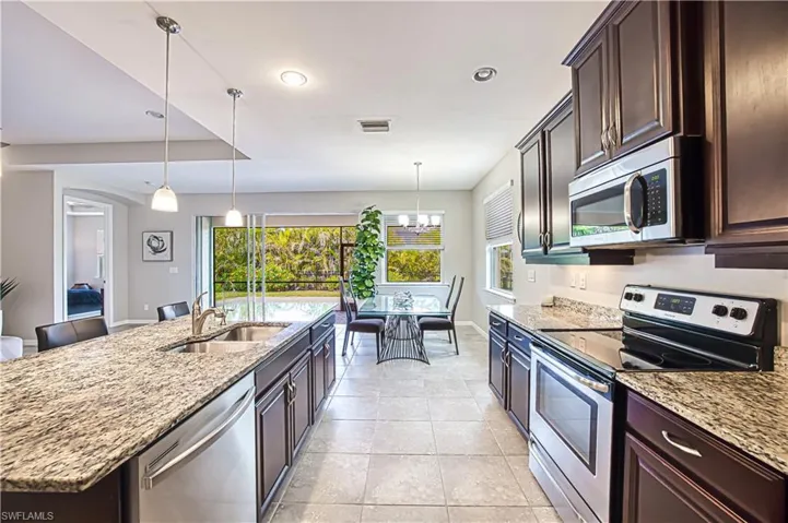 Kitchen featuring sink, decorative light fixtures, appliances with stainless steel finishes, an island with sink, and light stone countertops
