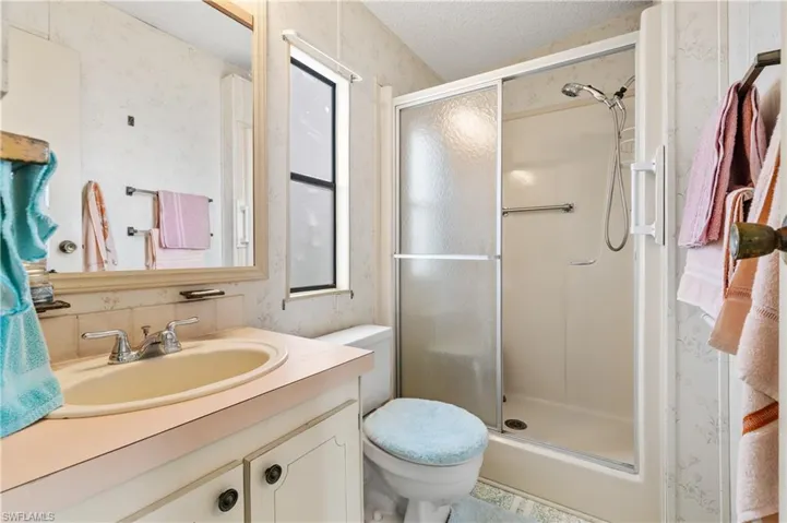 Bathroom with wallpapered walls, vanity, a stall shower, and a textured ceiling