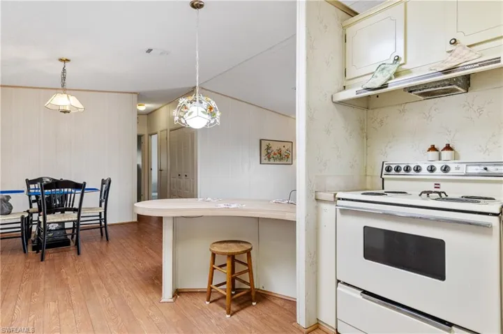 Kitchen featuring white electric range oven, a peninsula, light countertops, light wood finished floors, and a kitchen breakfast bar
