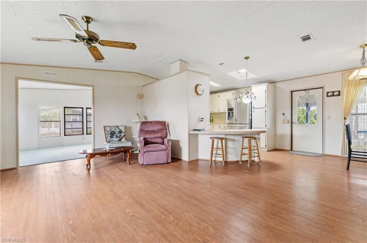 Living area with healthy amount of natural light, light wood-type flooring, ceiling fan, a textured ceiling, and ornamental molding