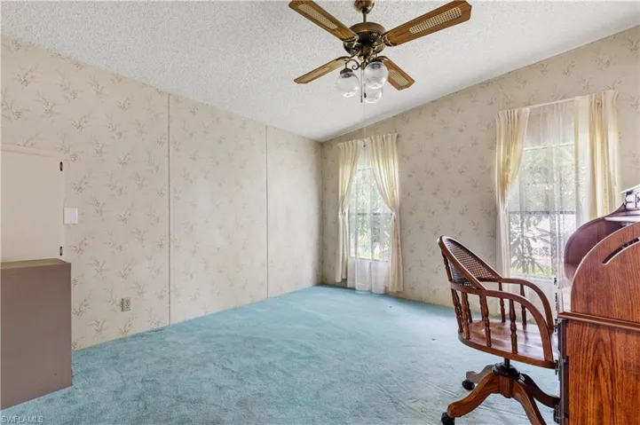 Carpeted office with wallpapered walls, a textured ceiling, and a ceiling fan