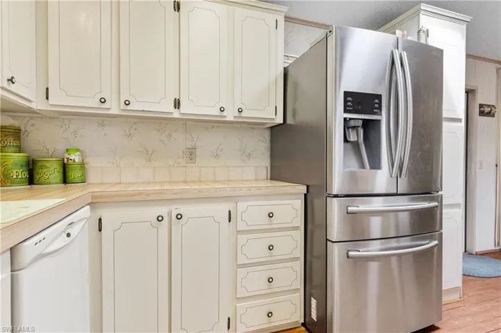 Kitchen with wallpapered walls, light countertops, stainless steel fridge with ice dispenser, white dishwasher, and white cabinets