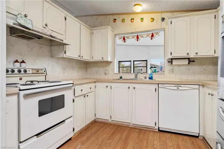 Kitchen with wallpapered walls, white appliances, light countertops, under cabinet range hood, and light wood-type flooring