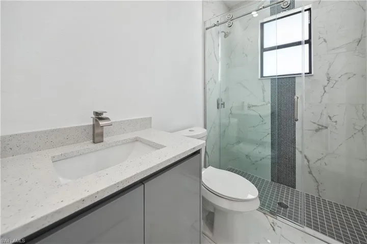 Bathroom with toilet, a marble finish shower, and vanity