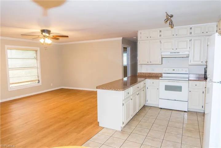 Kitchen with white appliances, a peninsula, under cabinet range hood, light tile patterned floors, and white cabinetry