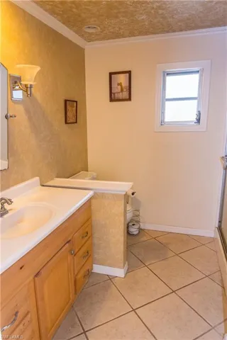 Full bath featuring vanity, crown molding, and light tile patterned floors