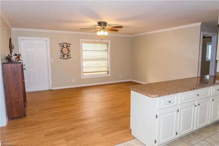 Kitchen featuring light stone counters, a ceiling fan, ornamental molding, light wood-type flooring, and white cabinetry