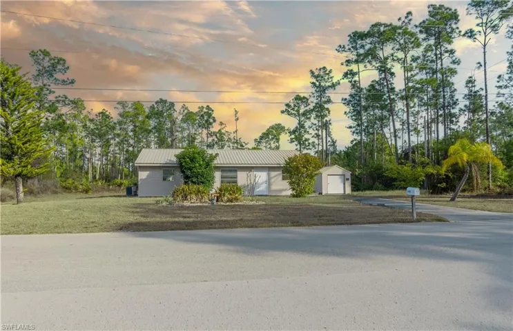 Ranch-style home featuring driveway, a garage, an outbuilding, a metal roof, and view of scattered trees
