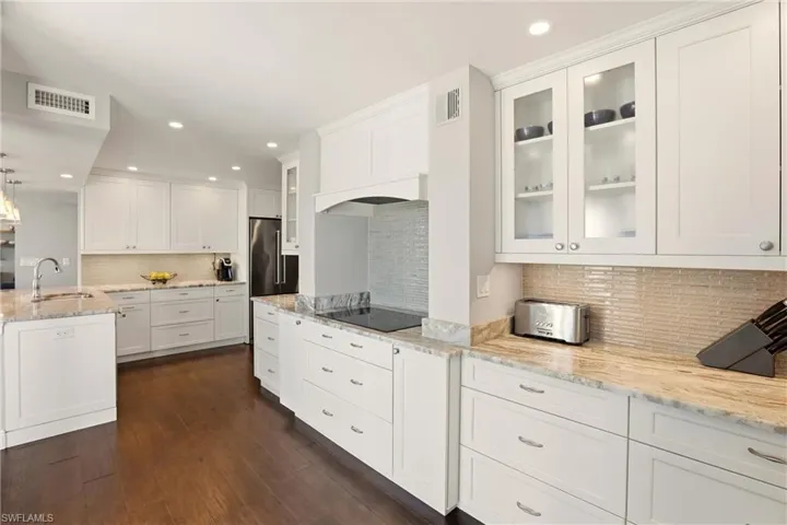 Kitchen with white cabinets, decorative light fixtures, light stone countertops, recessed lighting, and decorative backsplash