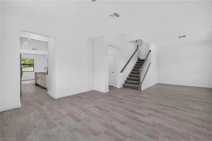 Neutral tone wall paint, wood-look tile flooring, carpeted staircase with dark handrails, recessed lighting, and a kitchen island with a single basin sink