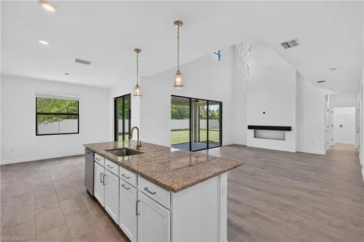 Kitchen island with granite countertop, white cabinetry, and stainless steel sink