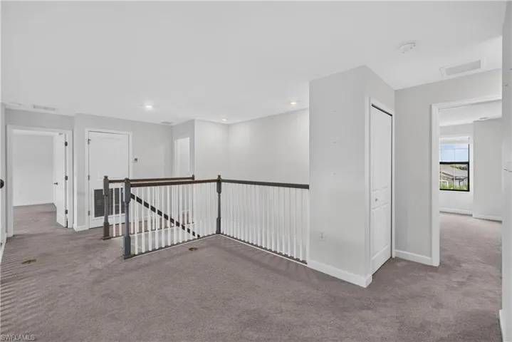 Carpeted upper level with painted white walls, recessed lighting, and white spindle railing with dark wood-finish handrails