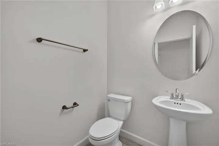 Pedestal sink with chrome fixtures, wall-mounted oval mirror, and white toilet