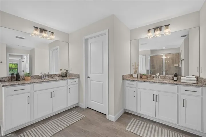 Dual vanities featuring granite countertops, undermount sinks, and white cabinetry with brushed nickel hardware