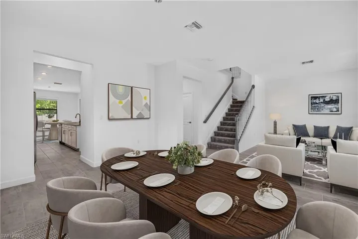 Spacious dining area with wood-finish flooring, an adjacent kitchen featuring a stainless steel sink, and a staircase with a dark wood handrail