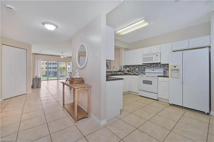 Kitchen featuring white cabinetry, dark countertops, a patterned tile backsplash, and white built-in appliances, set against ceramic tile flooring