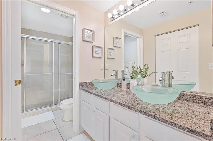 Dual glass vessel sinks, stone-finish countertop, white cabinetry, wall-to-wall mirror, and a walk-in shower with sliding glass doors