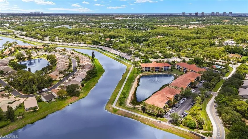 Aerial perspective featuring multi-unit residential structures, prominent water features with fountains, paved parking areas, and mature tree-lined landscaping