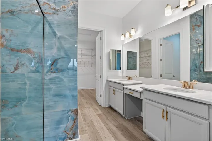 Full bathroom featuring a spacious closet, a marble finish shower, double vanity, and light wood finished floors