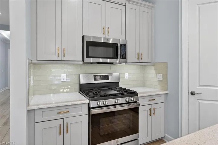 Kitchen with stainless steel appliances, tasteful backsplash, and light stone counters