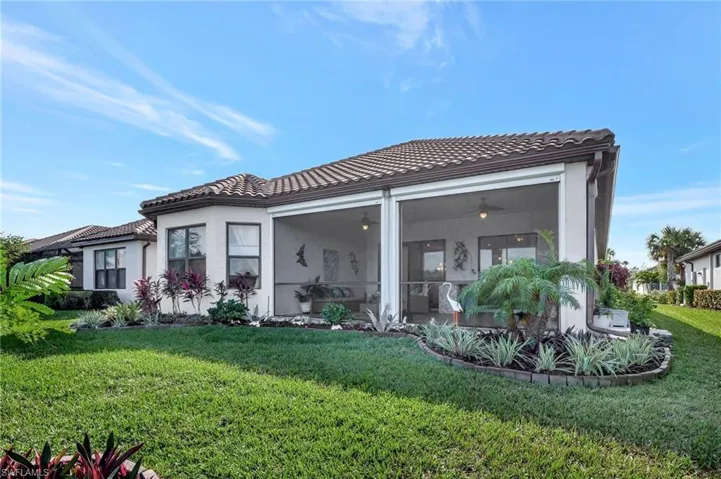 Back of property featuring a lawn, a sunroom, stucco siding, and a tile roof