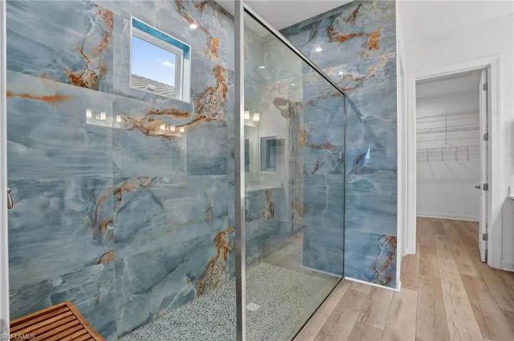 Full bath with a marble finish shower, wood finished floors, and a spacious closet