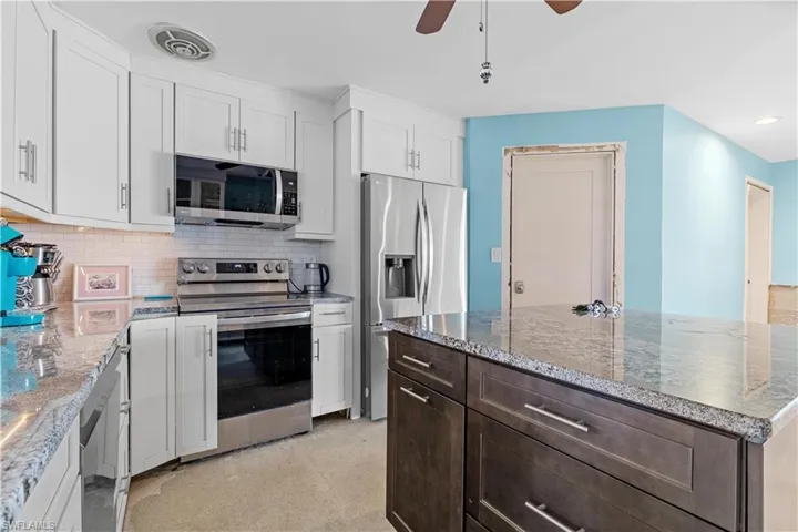 Kitchen featuring backsplash, white cabinets, ceiling fan, light stone countertops, and stainless steel appliances